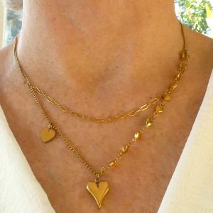 Gouden stainless steel ketting met dubbele lagen, versierd met kleine hartjes en een opvallende hartjeshanger. Een elegant en romantisch sieraad dat perfect past bij elke gelegenheid.