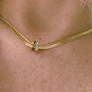 Gouden stainless steel ketting met dubbele ringen, waarvan één ring is bezet met fonkelende zirkonia steentjes. De ketting heeft een moderne, dubbele kettingstructuur en straalt elegantie en stijl uit